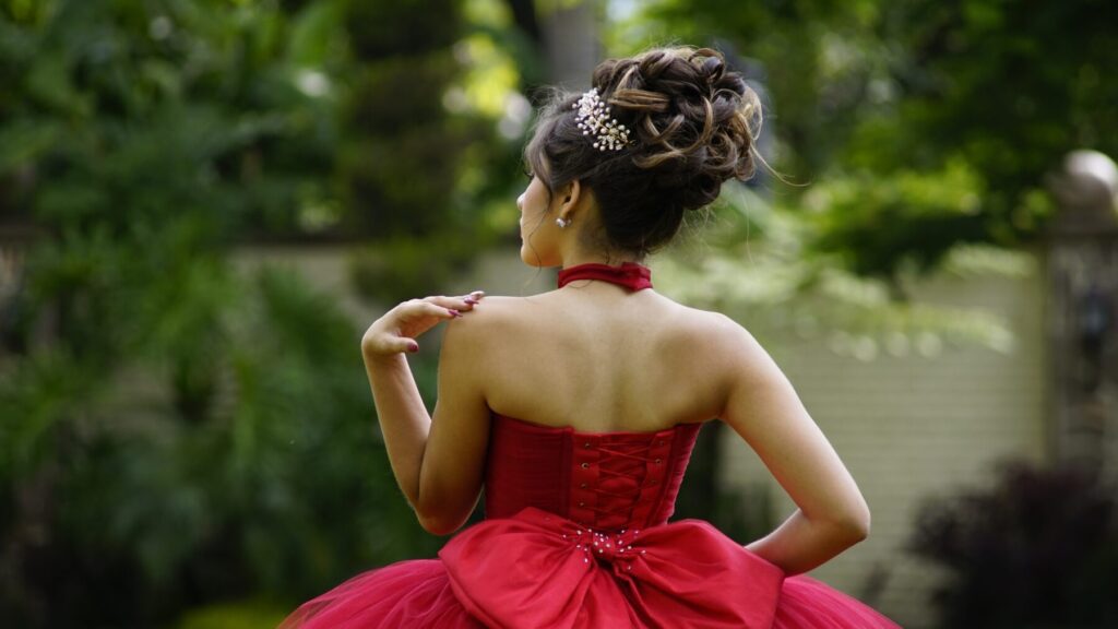 Femme portant une robe rouge avec une coiffure élégante, posant dans un jardin verdoyant.