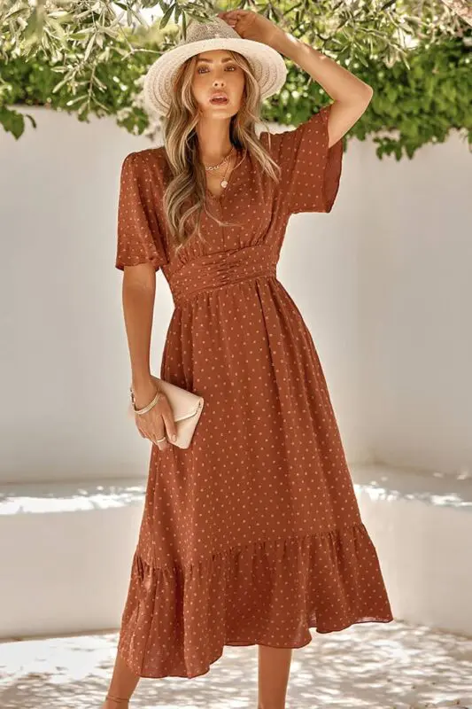 Femme en robe à pois longue marron, look bohème avec un chapeau et des accessoires.