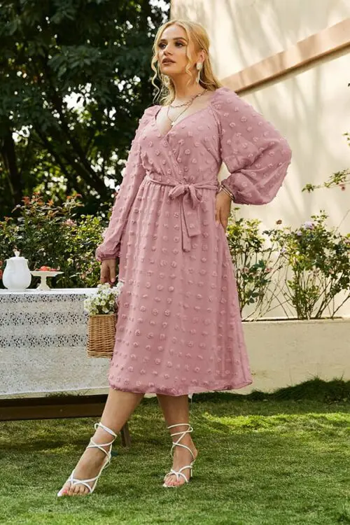 Robe à pois midi rose avec manches longues et ceinture, look chic et raffiné.