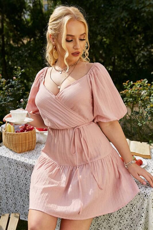 Jeune femme en robe bohème grande taille rose poudré à manches bouffantes, style portefeuille